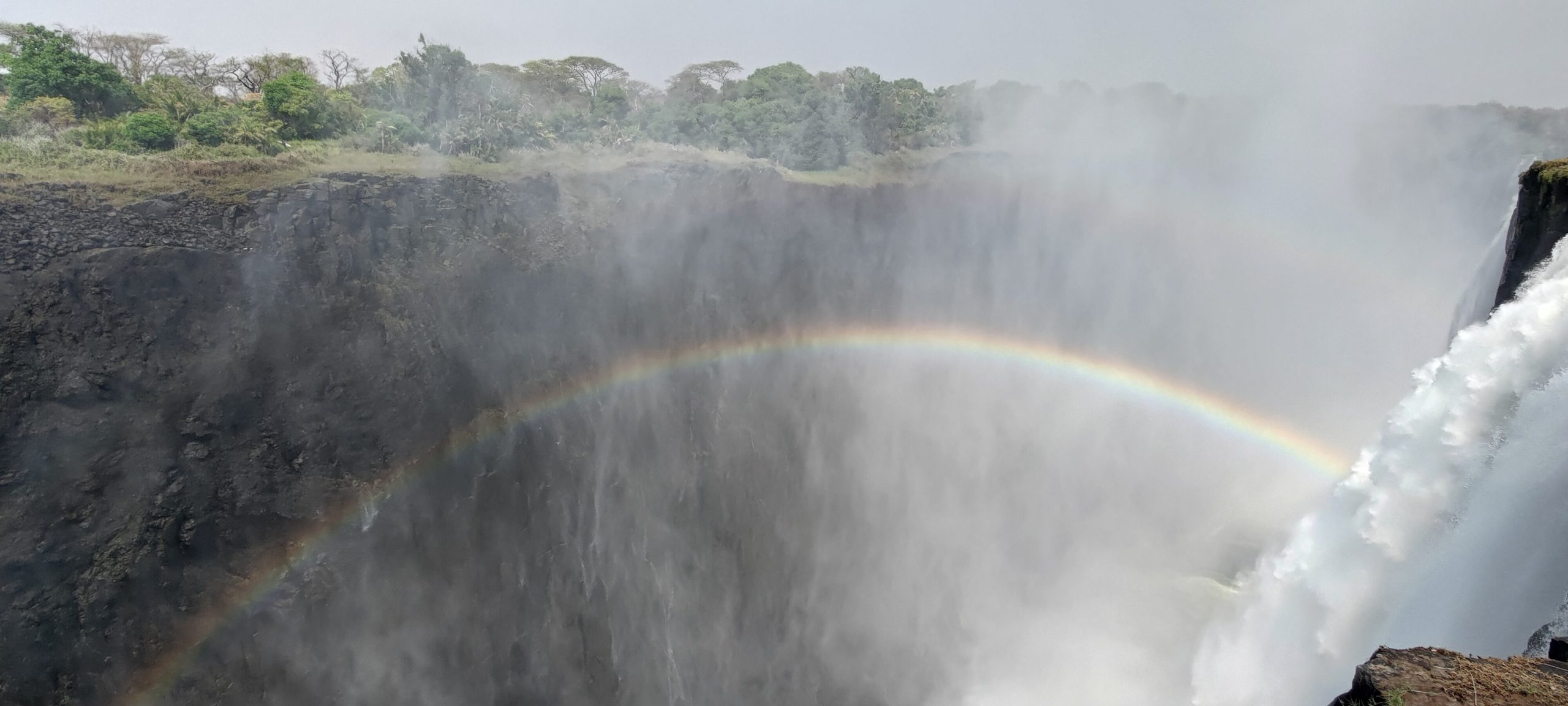 Wasserfall mit Regenbogen und Infinity-Pool im Hintergrund.