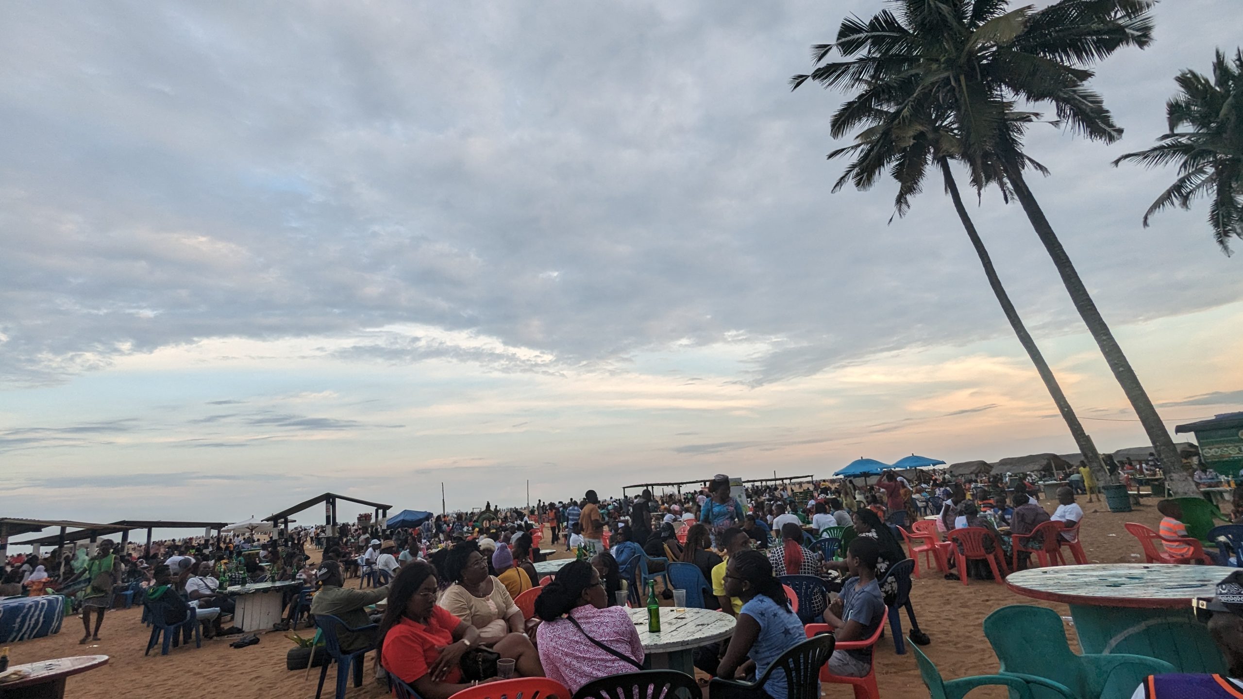 Bunte Strandkulisse in Togo mit Menschen, Palmen und Meer bei Sonnenuntergang.