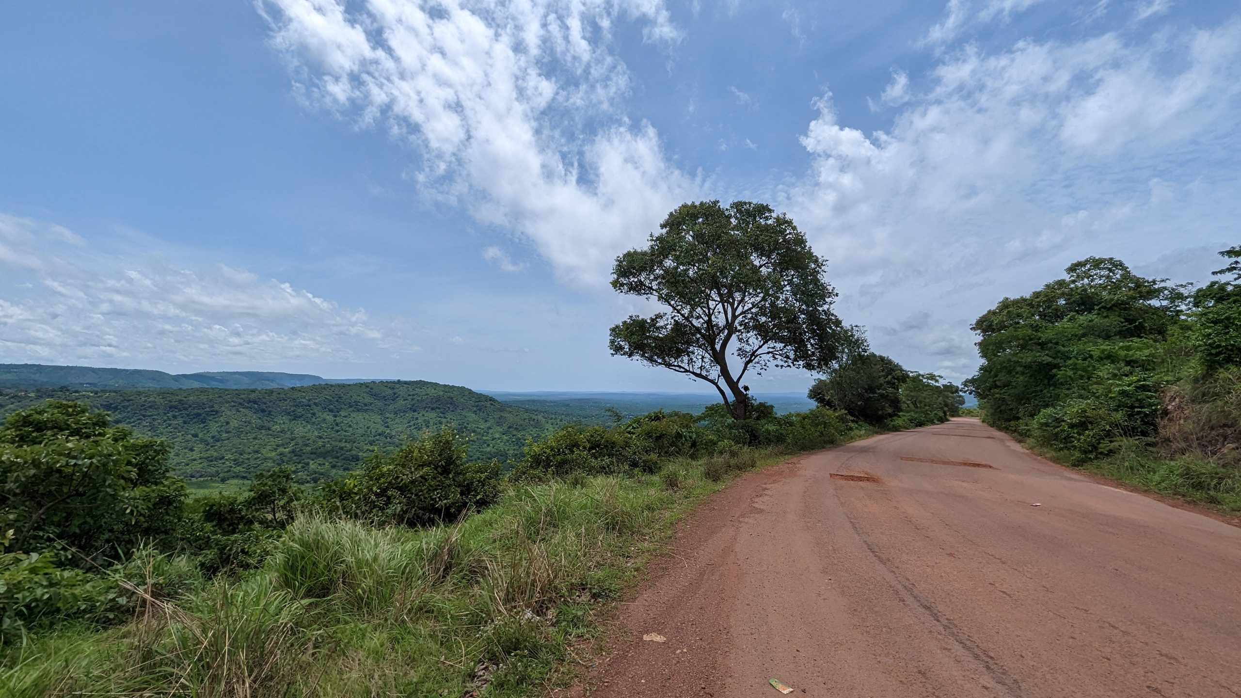 Schmale Straße in afrikanischer Landschaft mit Baum und Himmel.