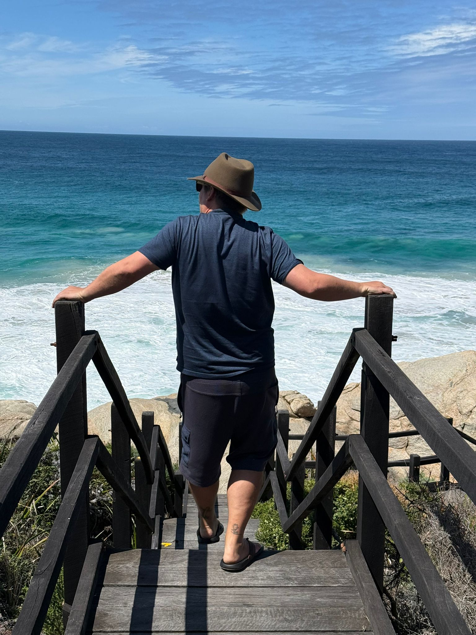 Mann in Unbound Merino T-Shirt am Strand, Blick aufs Meer.