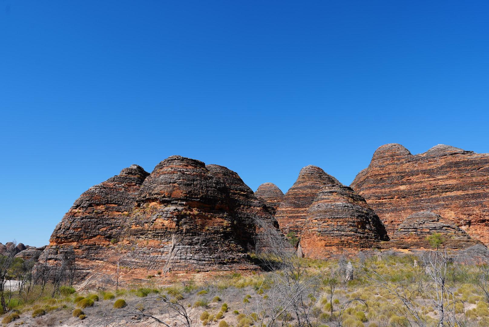Felsen im australischen Outback mit rotbraunen Schichten unter klarem blauen Himmel.